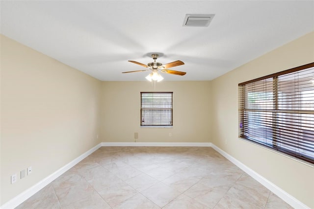 empty room featuring visible vents, a ceiling fan, and baseboards