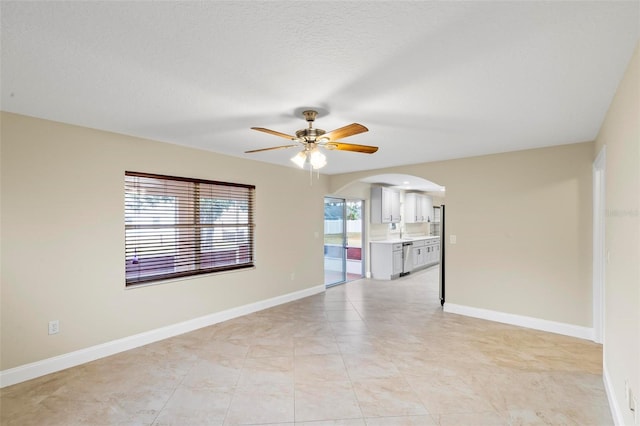 empty room featuring baseboards, arched walkways, a textured ceiling, and a ceiling fan