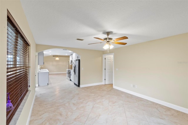 unfurnished room featuring a sink, baseboards, arched walkways, and a textured ceiling