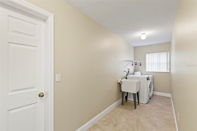 washroom with laundry area, washing machine and dryer, a textured ceiling, and baseboards