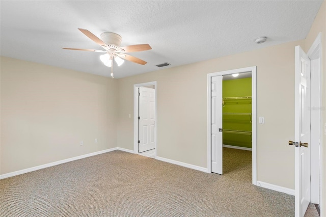 unfurnished bedroom with visible vents, a textured ceiling, carpet floors, baseboards, and a spacious closet