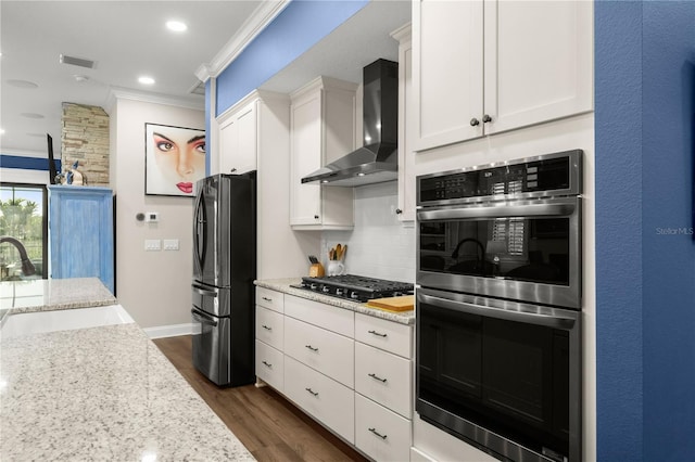 kitchen featuring ornamental molding, a sink, stainless steel appliances, wall chimney exhaust hood, and decorative backsplash