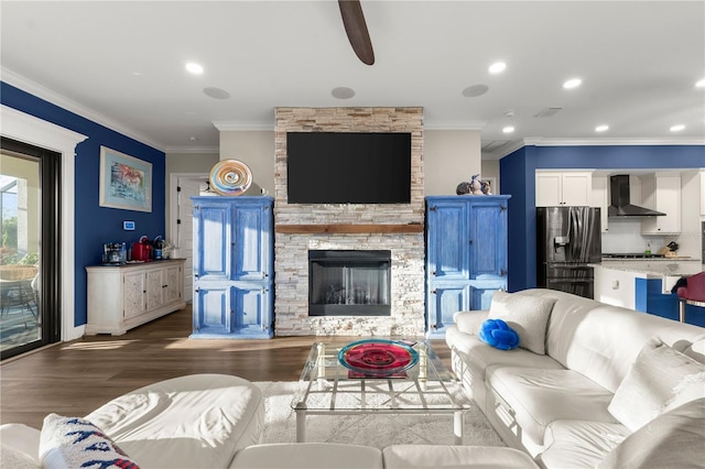 living room with a stone fireplace, crown molding, recessed lighting, and wood finished floors