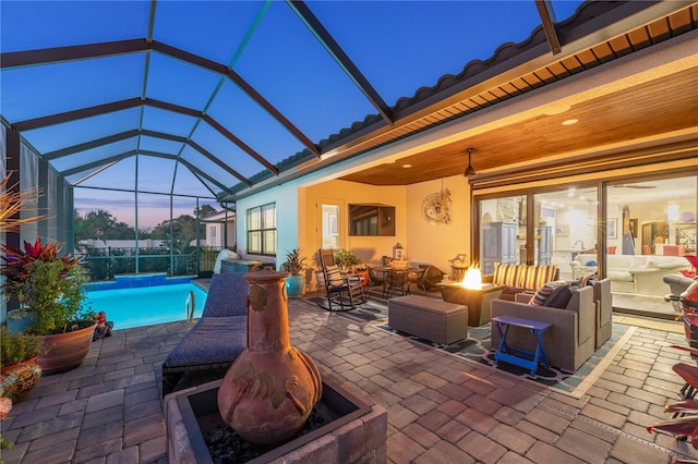 patio terrace at dusk featuring glass enclosure, a fire pit, and an outdoor pool