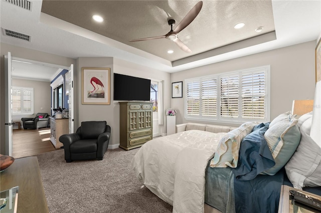 carpeted bedroom featuring a raised ceiling, recessed lighting, and visible vents