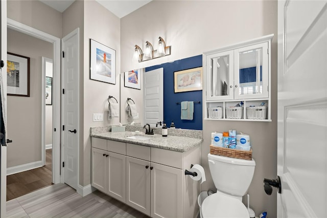 bathroom with vanity, toilet, wood finished floors, and baseboards