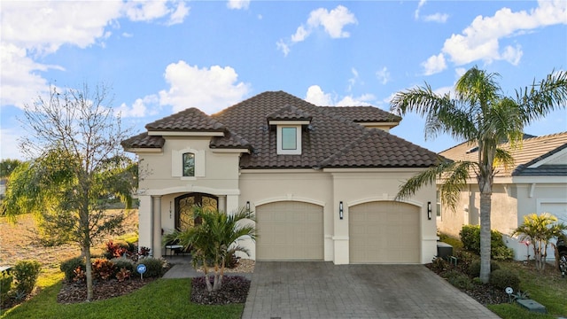 mediterranean / spanish-style home featuring a tiled roof, stucco siding, an attached garage, and decorative driveway