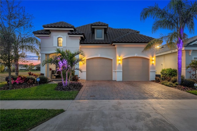 mediterranean / spanish house featuring stucco siding, an attached garage, driveway, and a tile roof