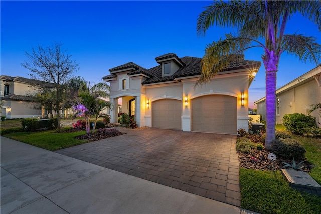 mediterranean / spanish-style house featuring decorative driveway, a tile roof, an attached garage, and stucco siding