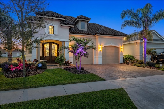 mediterranean / spanish home featuring a tile roof, stucco siding, french doors, decorative driveway, and a garage