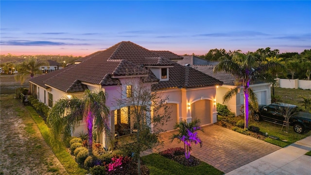 view of front of house with a tile roof, decorative driveway, a garage, and stucco siding