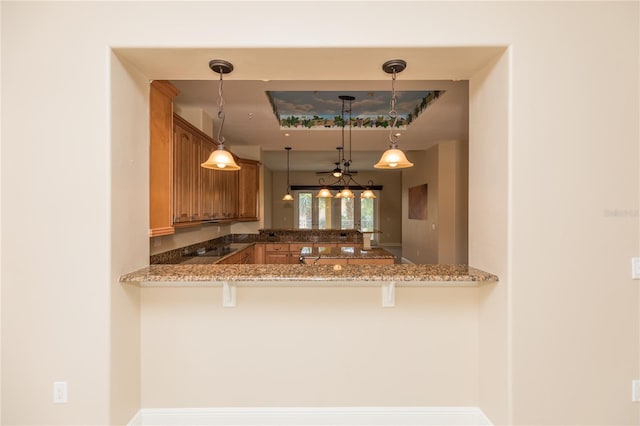 kitchen with a peninsula, a breakfast bar area, brown cabinetry, black electric stovetop, and hanging light fixtures