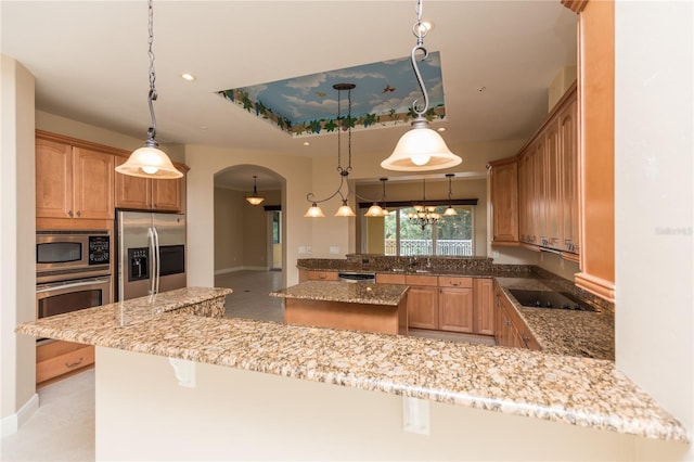 kitchen featuring a tray ceiling, appliances with stainless steel finishes, a peninsula, arched walkways, and a sink