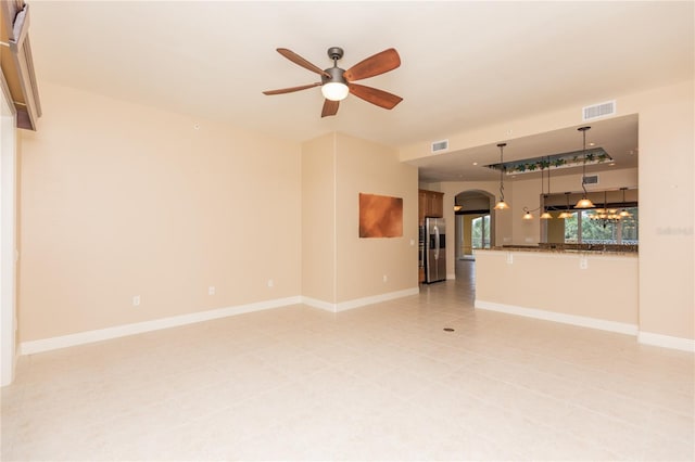 unfurnished living room featuring baseboards, arched walkways, visible vents, and ceiling fan