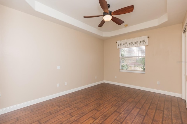 unfurnished room featuring a tray ceiling, dark wood-style floors, baseboards, and ceiling fan