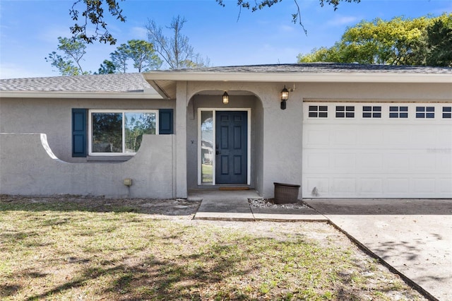 property entrance featuring a shingled roof, concrete driveway, an attached garage, and stucco siding