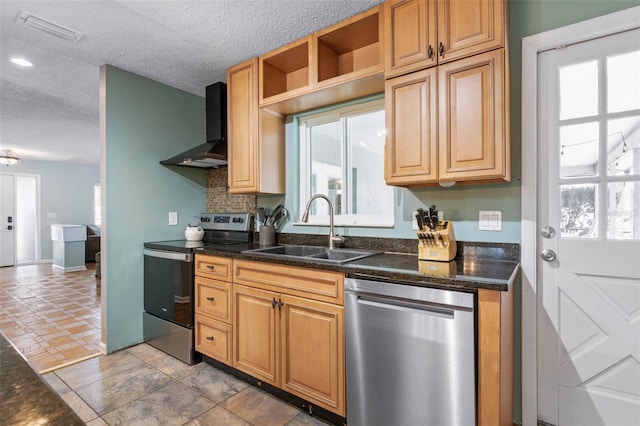 kitchen featuring visible vents, wall chimney range hood, appliances with stainless steel finishes, a textured ceiling, and a sink