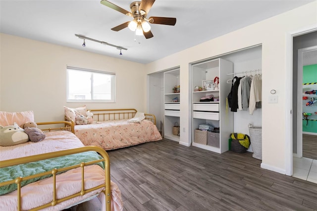 bedroom featuring multiple closets, wood finished floors, rail lighting, baseboards, and ceiling fan