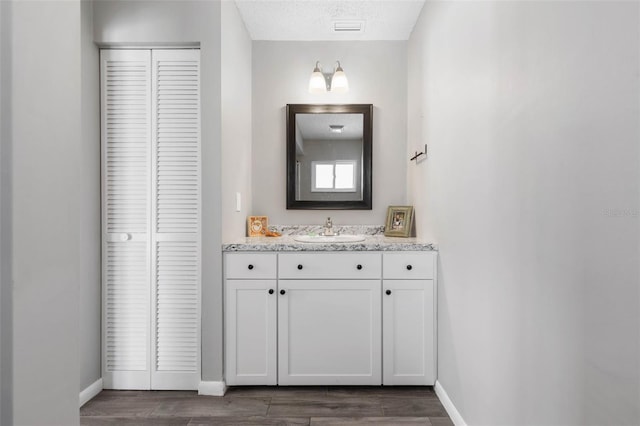 bathroom with vanity, wood finished floors, visible vents, baseboards, and a closet