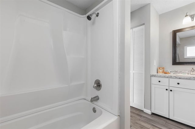 full bath featuring a textured ceiling, wood finished floors, a closet, bathtub / shower combination, and vanity