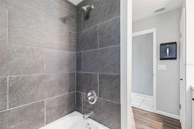 bathroom featuring visible vents, a textured ceiling, wood finished floors,  shower combination, and baseboards