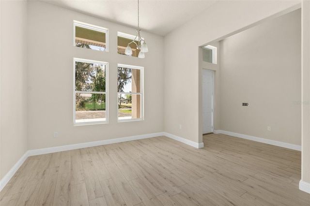 empty room with baseboards, light wood-type flooring, and an inviting chandelier