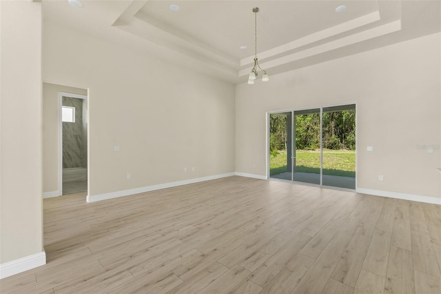 empty room with a raised ceiling, a high ceiling, baseboards, and light wood finished floors