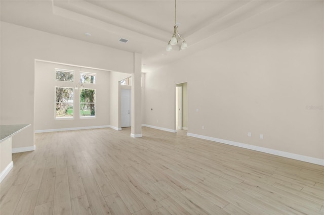 unfurnished room featuring visible vents, baseboards, a chandelier, a tray ceiling, and light wood-style floors