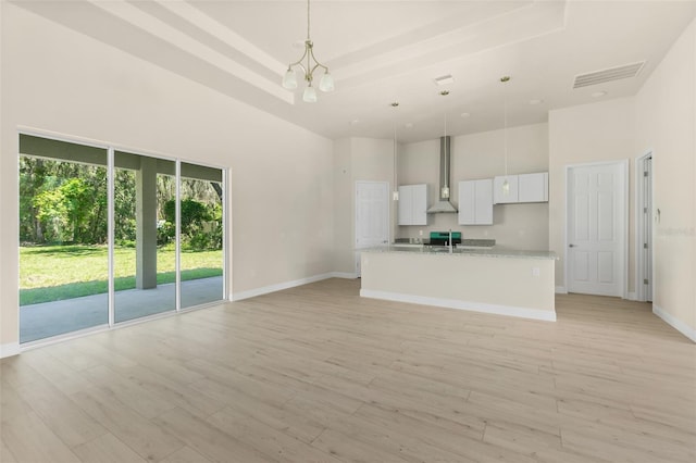 unfurnished living room with visible vents, light wood finished floors, a tray ceiling, a towering ceiling, and a chandelier