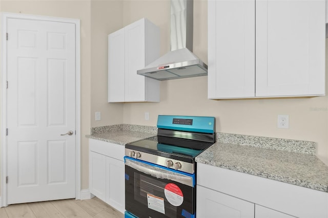 kitchen with light stone counters, white cabinets, electric stove, and wall chimney range hood