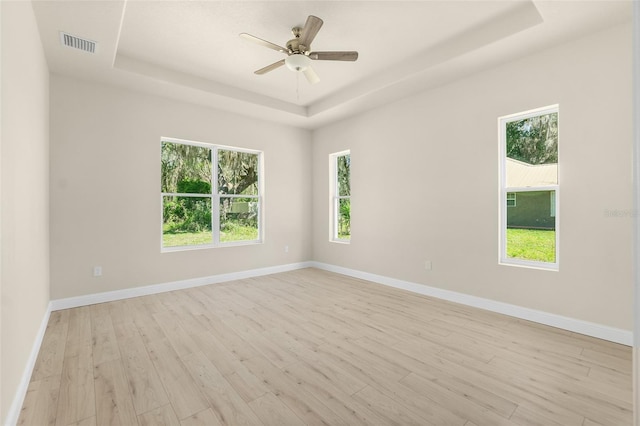 empty room with a tray ceiling, plenty of natural light, visible vents, and light wood finished floors