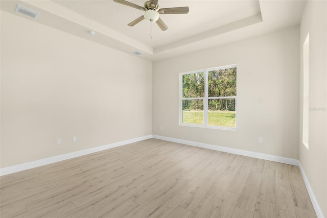 unfurnished room featuring visible vents, light wood-style flooring, a raised ceiling, and baseboards