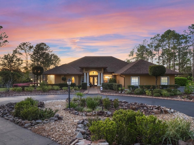 view of front of house featuring curved driveway, roof with shingles, and stucco siding