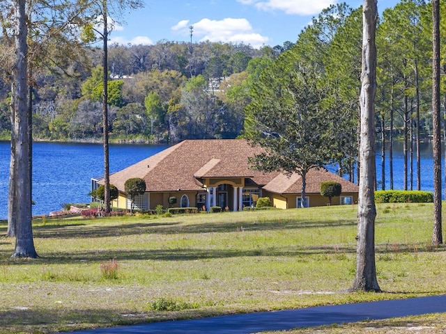 exterior space featuring stucco siding, a water view, a wooded view, and a front lawn