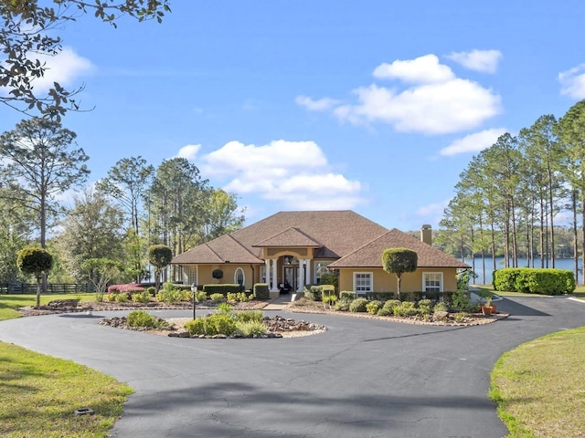 view of front of home featuring stucco siding, a water view, curved driveway, and a chimney