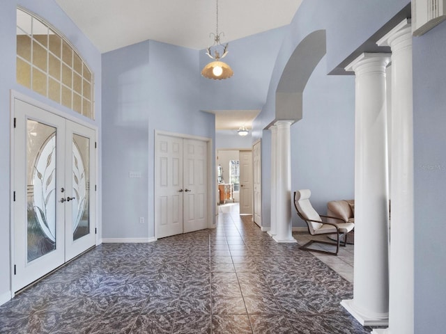 foyer entrance featuring french doors, arched walkways, baseboards, a towering ceiling, and ornate columns