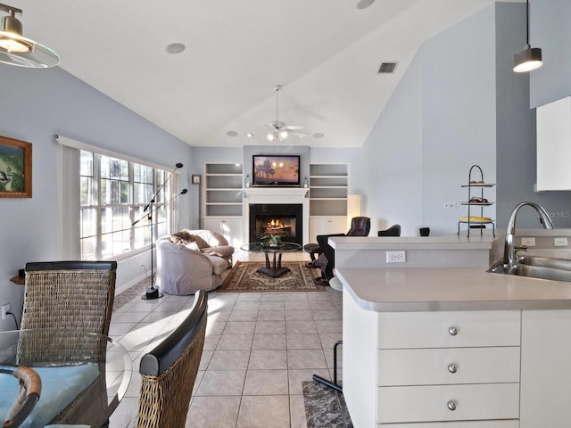 kitchen with a ceiling fan, a sink, built in features, light tile patterned floors, and lofted ceiling