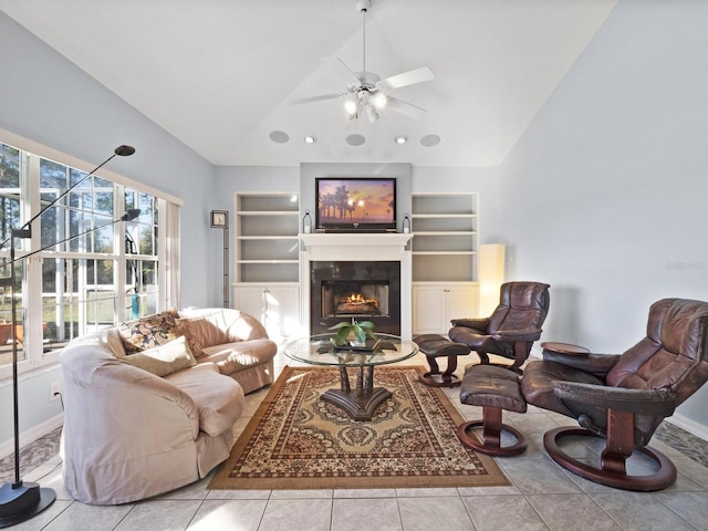 living room featuring built in shelves, lofted ceiling, ceiling fan, and a warm lit fireplace