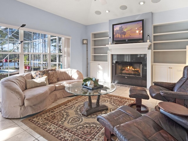 living area featuring a ceiling fan, a tiled fireplace, built in features, light tile patterned floors, and lofted ceiling