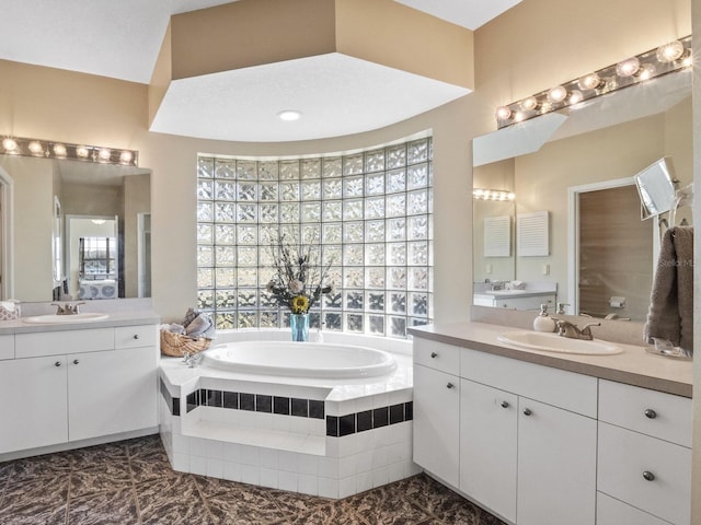 full bathroom featuring a garden tub, two vanities, and a sink