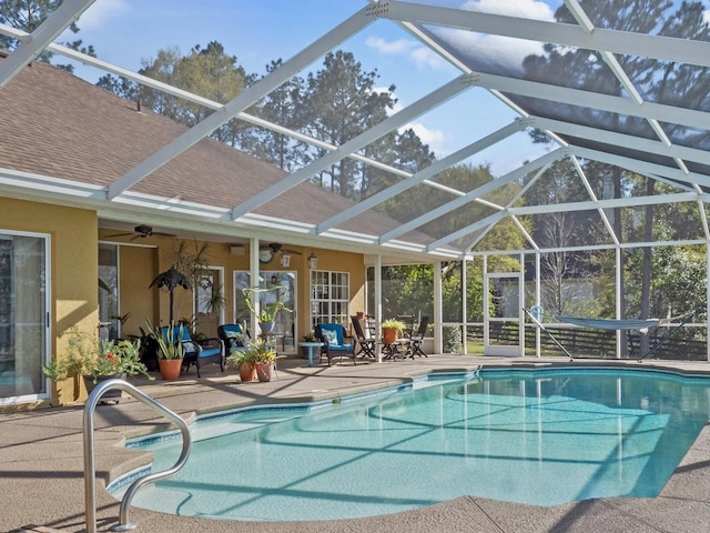 pool with glass enclosure, a patio, and a ceiling fan