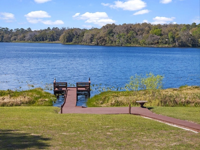 view of dock with a lawn, a water view, and a view of trees