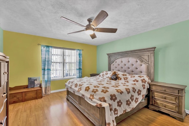 bedroom featuring ceiling fan, light wood-style flooring, baseboards, and a textured ceiling