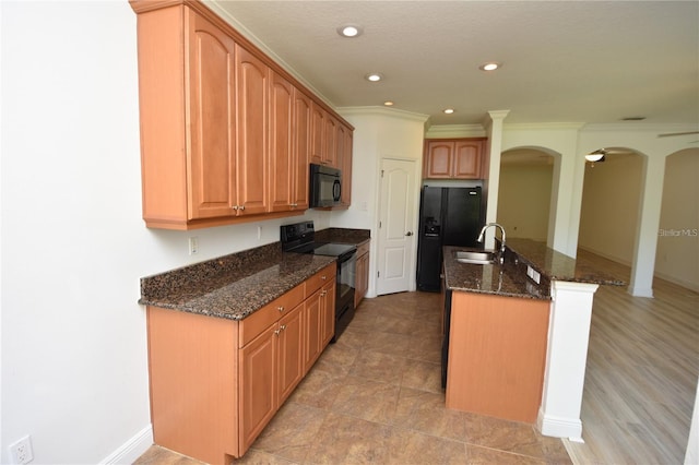 kitchen with dark stone counters, a kitchen island with sink, arched walkways, a sink, and black appliances