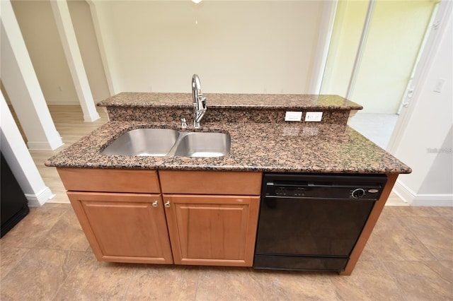 kitchen featuring dishwasher, dark stone countertops, an island with sink, and a sink