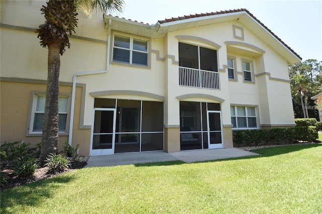 back of property with stucco siding, a yard, and a tile roof