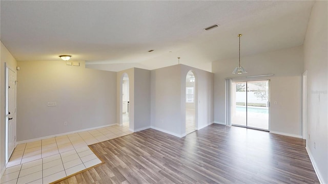 empty room with wood finished floors, baseboards, visible vents, arched walkways, and vaulted ceiling