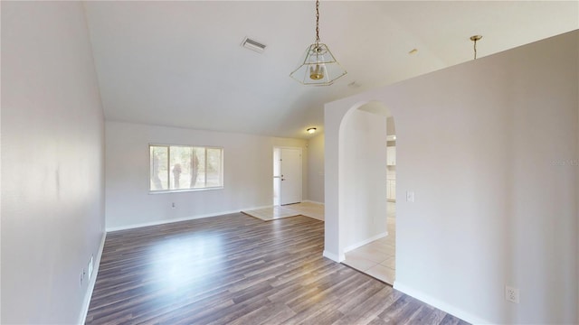 spare room with wood finished floors, arched walkways, visible vents, and baseboards