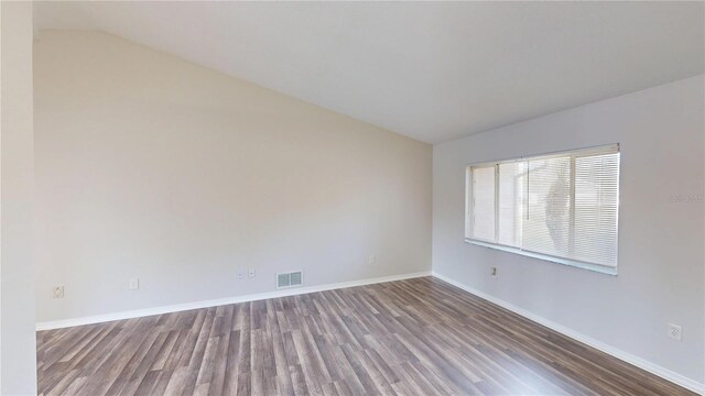 spare room featuring visible vents, baseboards, wood finished floors, and vaulted ceiling