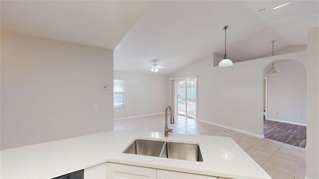 kitchen with light tile patterned floors, arched walkways, a sink, vaulted ceiling, and pendant lighting